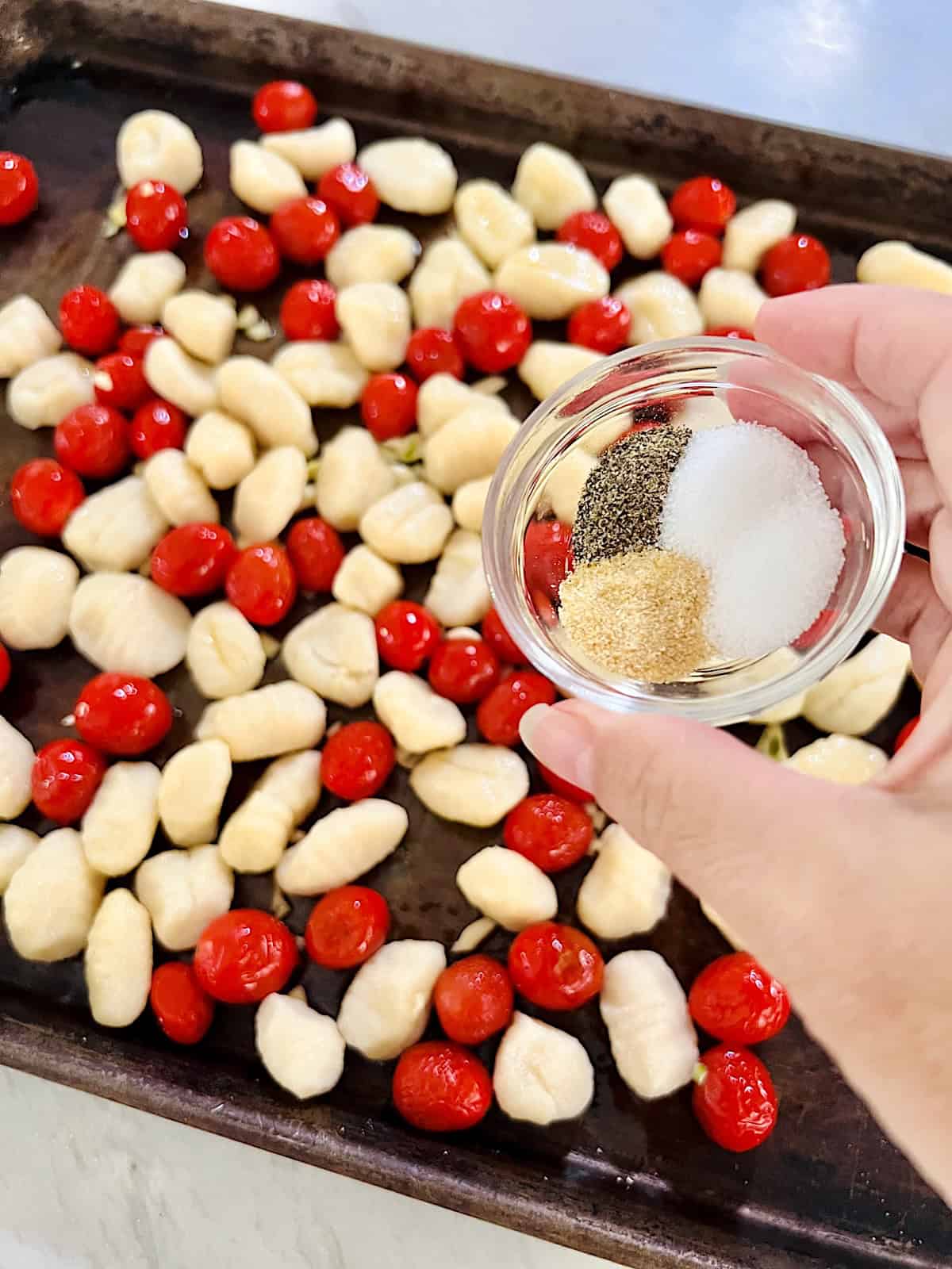 Adding spices to other ingredients on the baking sheet.