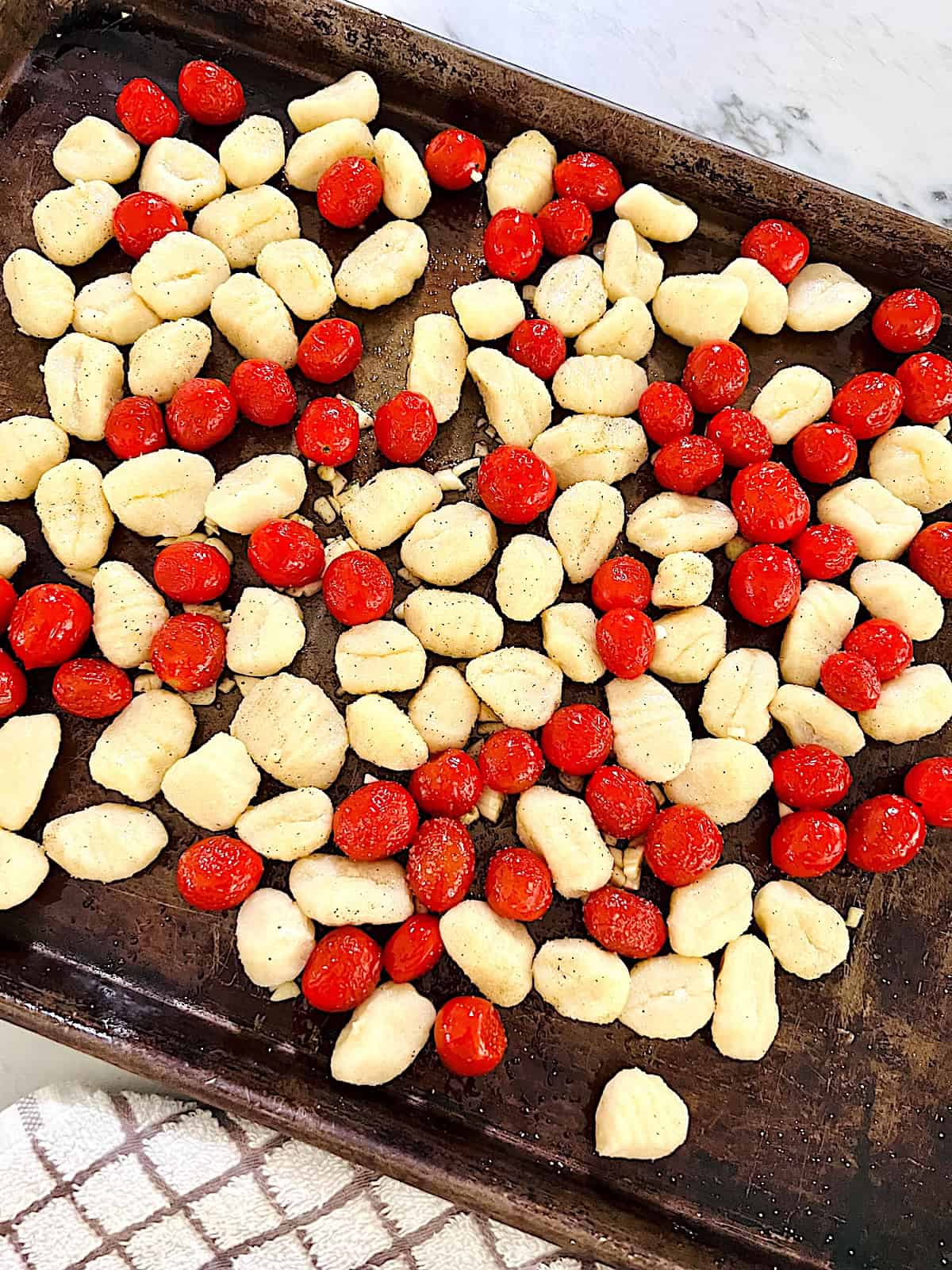 Sheet Pan Tomato Basil Gnocchi Raw cherry tomatoes potato gnocci and chopped garlic on a sheet pan.