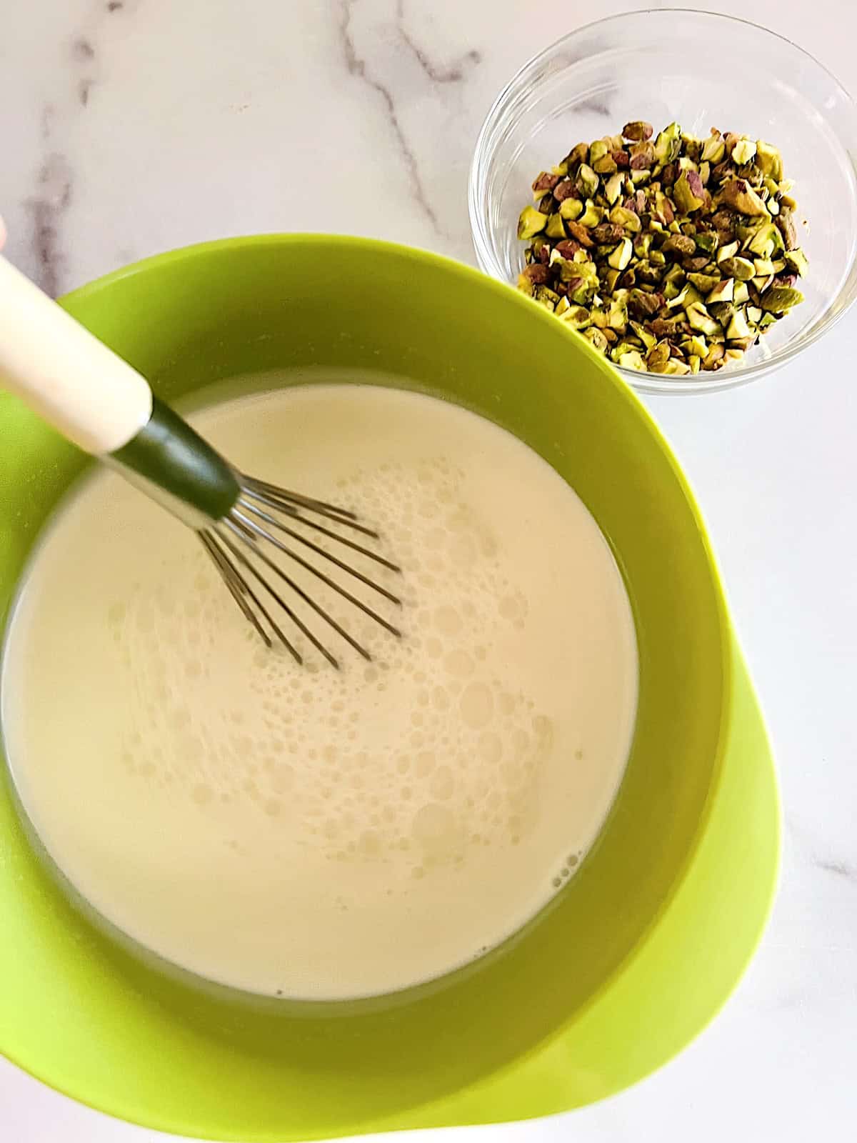 Ingredients whisked in bowl next to bowl of chopped salted roasted nuts.