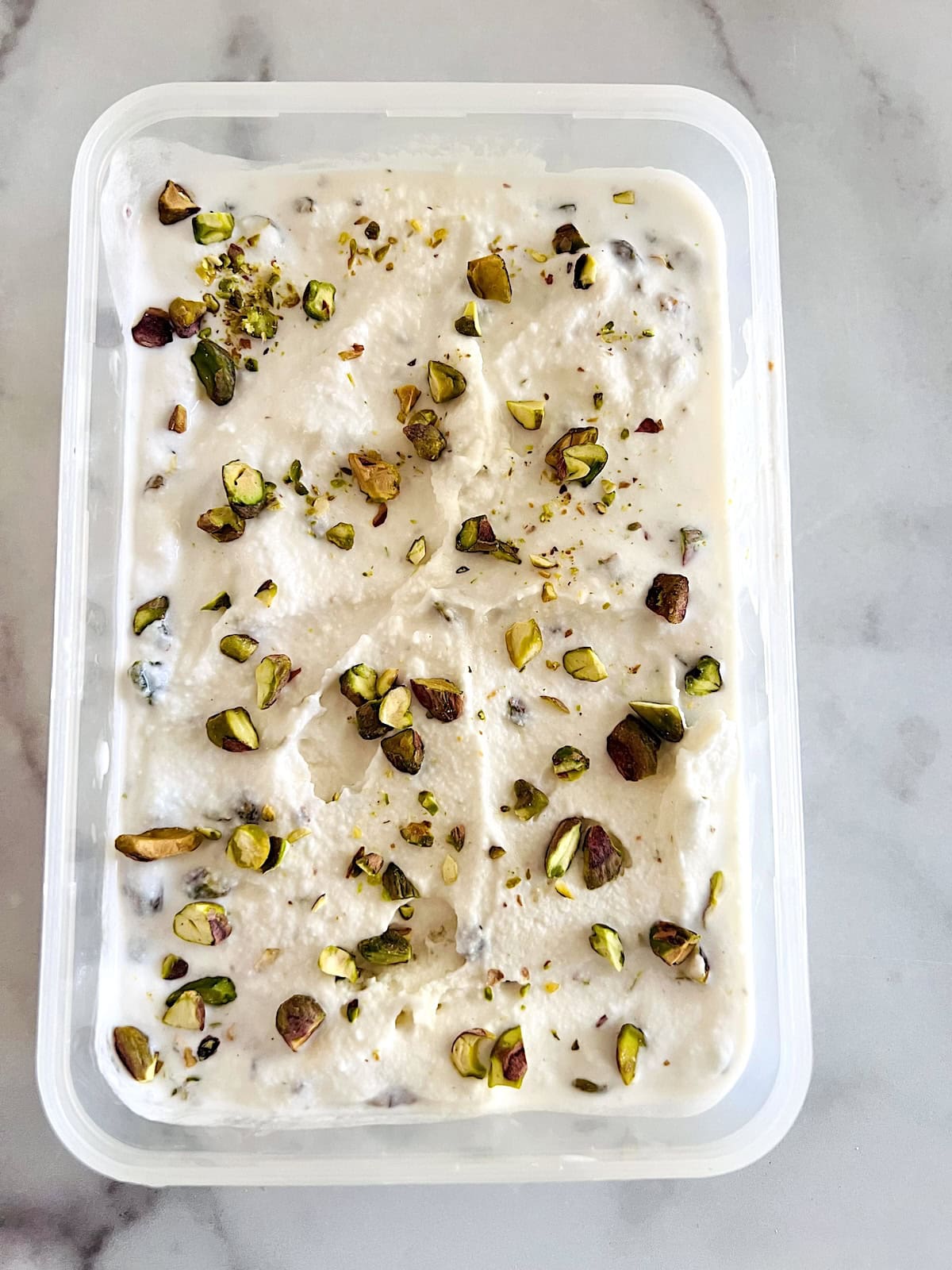Pistachio Ice Cream Layered and topped with more nuts ready to freeze.