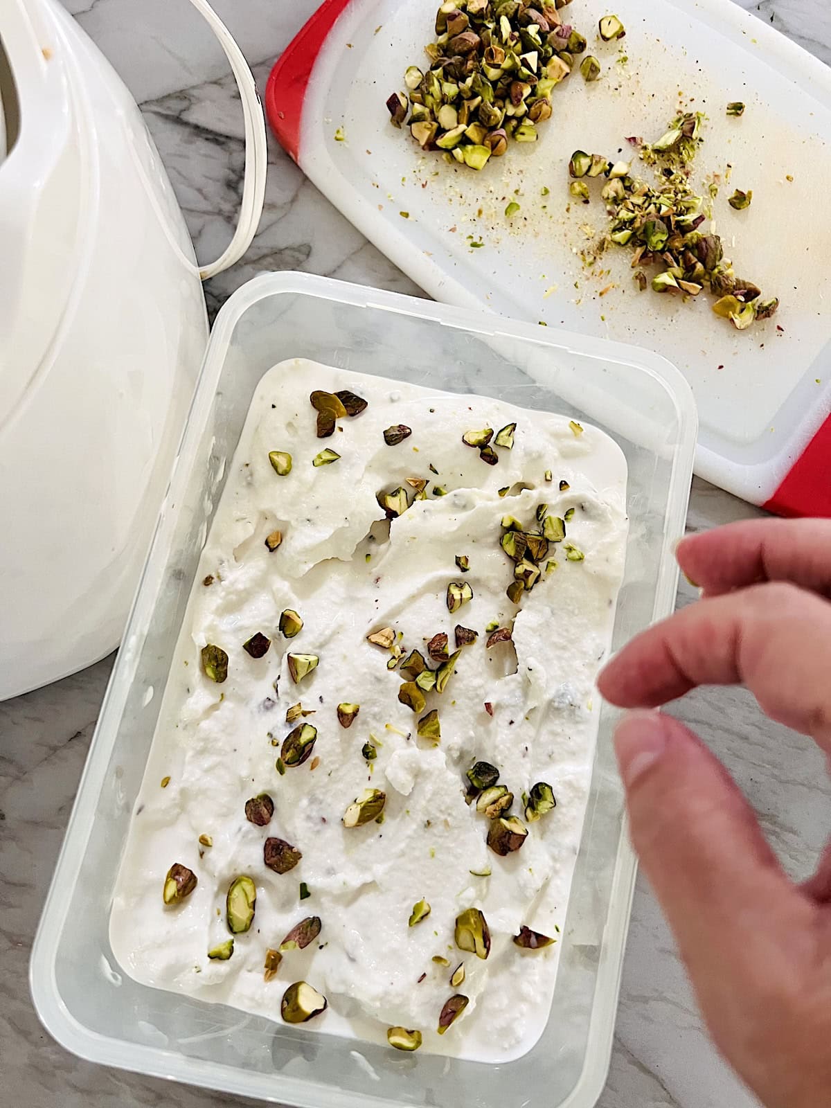 Pistachio Ice Cream Some in a container half way filled and sprinkling chopped nuts on top.
