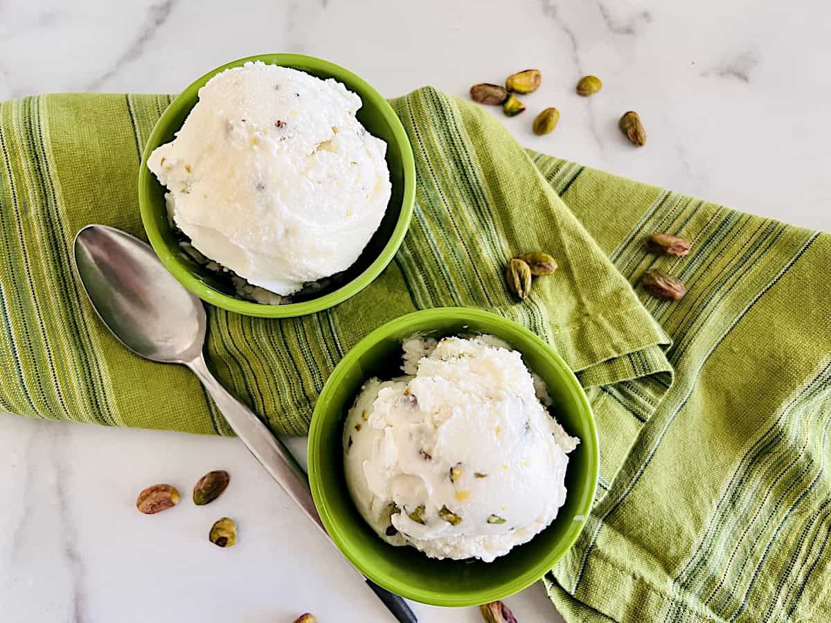 Two scoops of pistachio ice cream in green bowls next to scattered nuts.