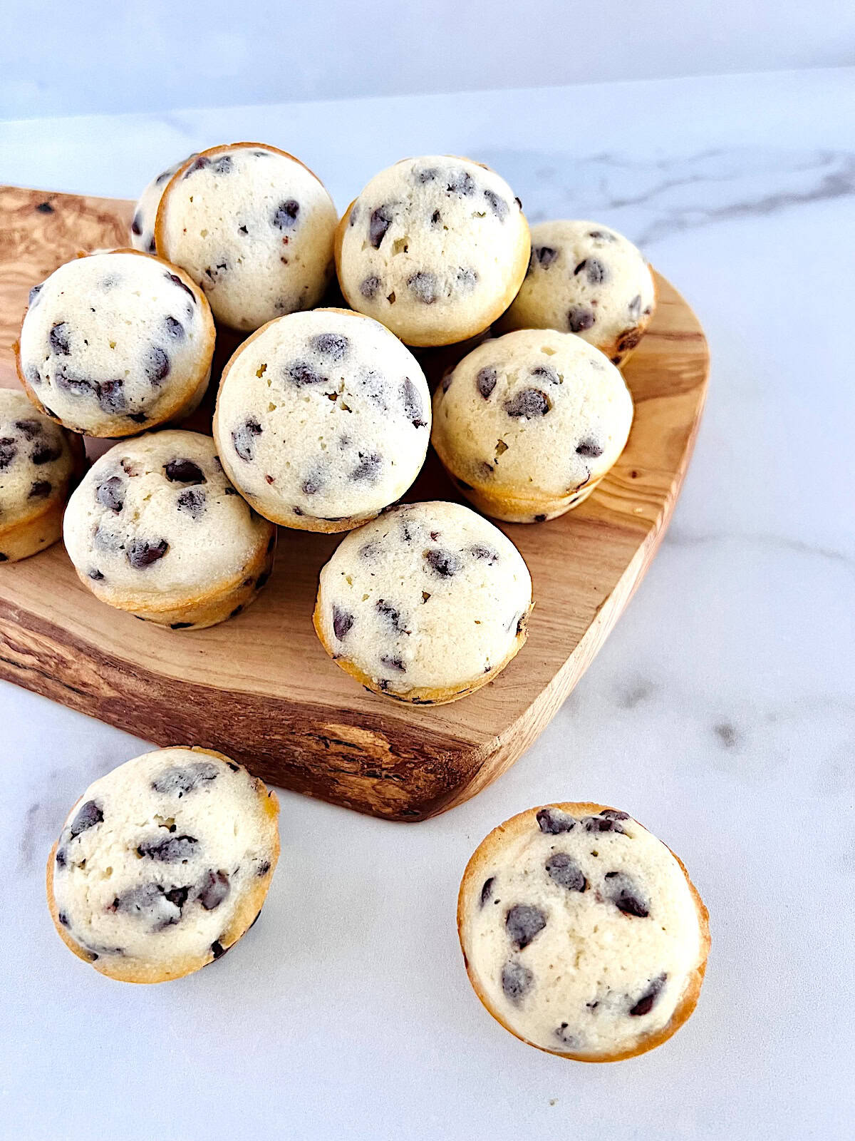 Mini Chocolate Chip Muffins loaded with semi sweet morsels stacked on a serving wooden board.