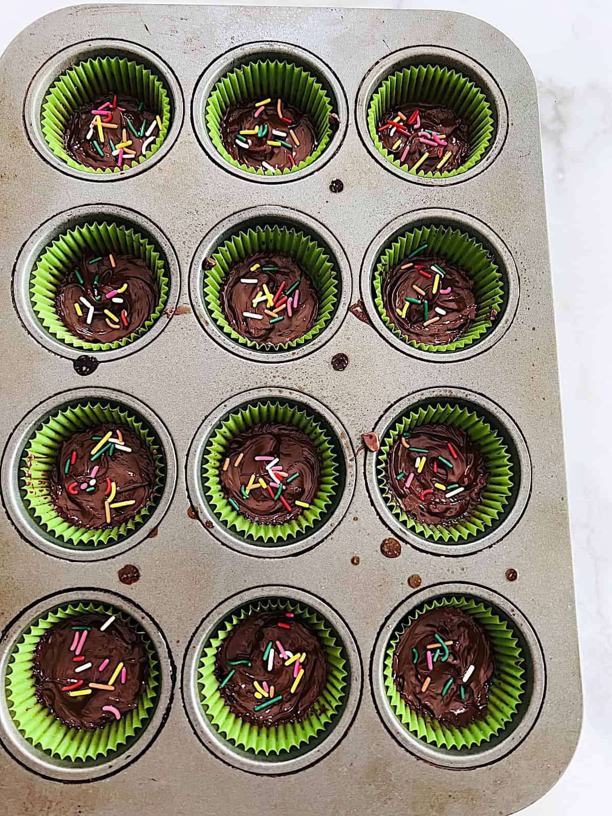 Ritz Cracker Toffee Cookies In Muffin Pan with melted chocolote on top and rainbow jimmy sprinkles.