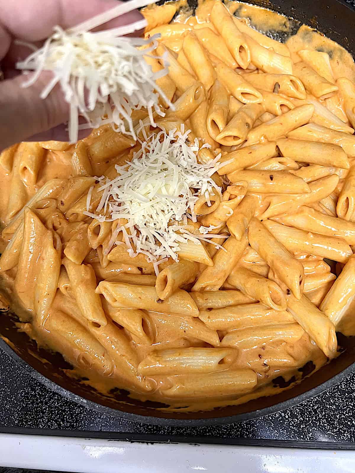 Penne alla Vodka adding parmesan over pasta in the skillet.