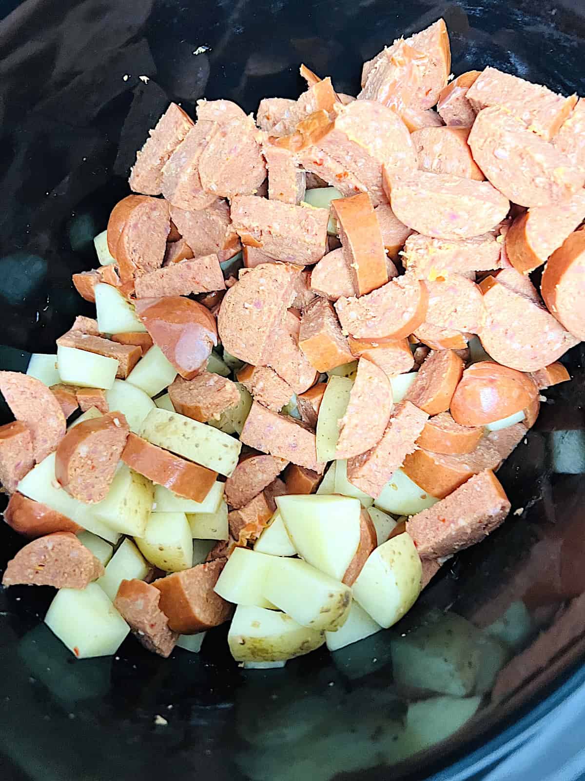 Chunks of links and potatoes in crockpot.