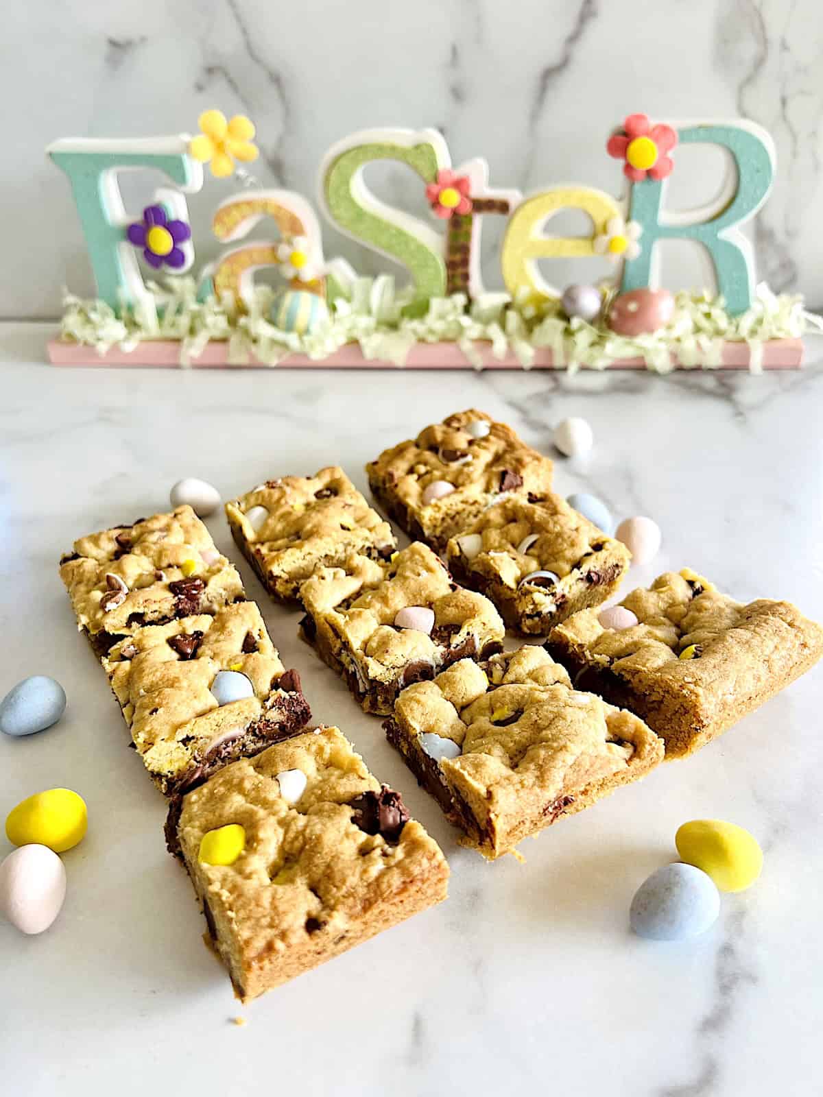 Cadbury Mini Egg Cookie Bars Cut bar cookies on the table with Easter sign in background.