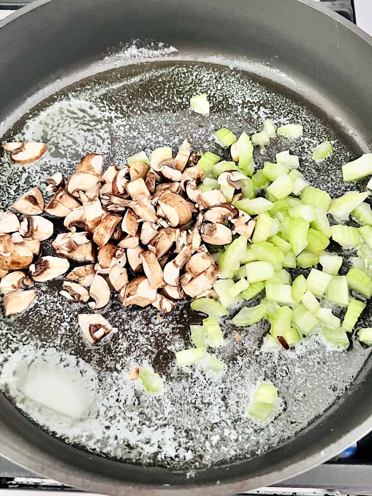 Diced vegetables cooking in melted butter in a pan.