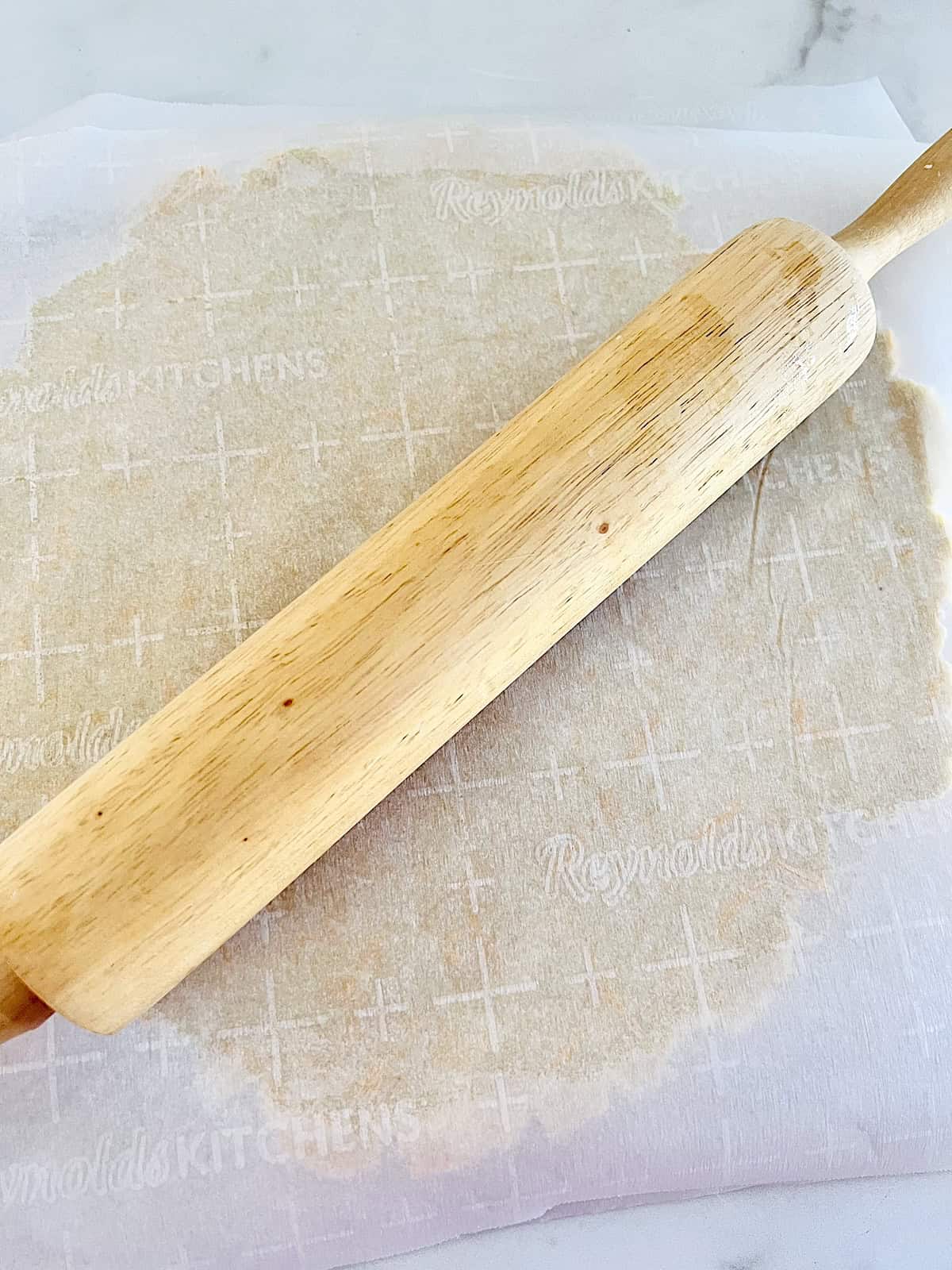 Savory Keto Pie Crust Rolled out between 2 pieces of parchment with rolling pin.