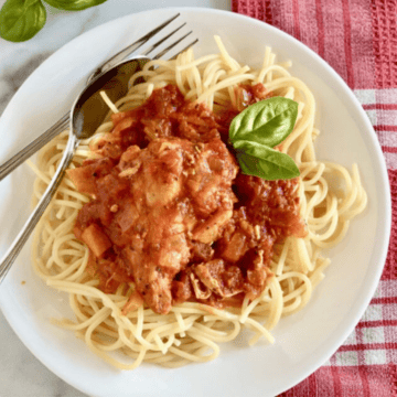 Slow Cooker Chicken Cacciatore with boneless skinless chicken and vegetables served over spaghetti on a plate.