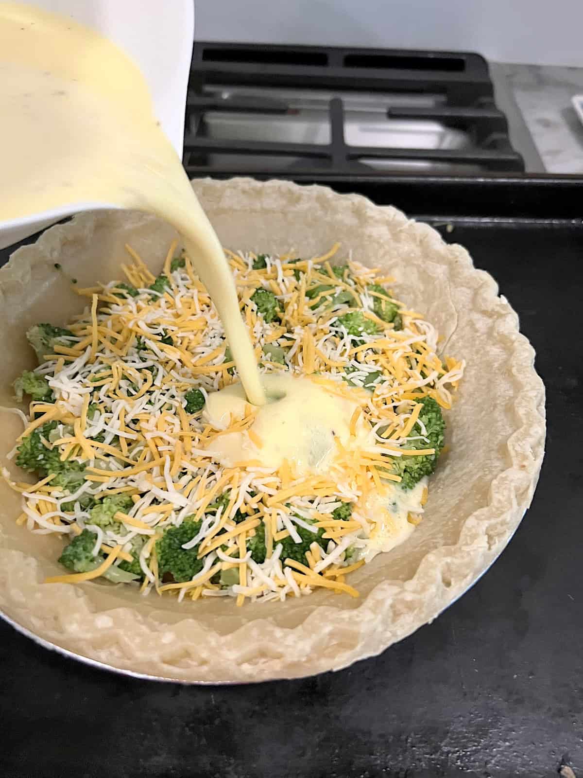 Broccoli Cheese Quiche Pouring egg custard over cheese and broccoli in parbaked pie crust.