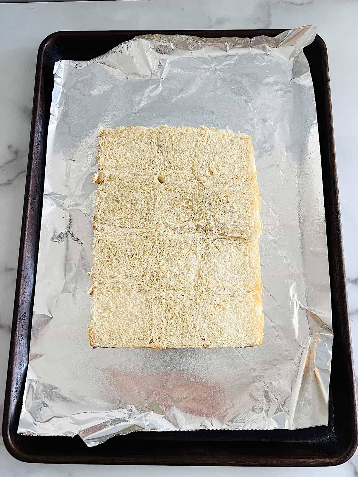 Bottom half of slider rolls cut horizontal on a baking sheet.