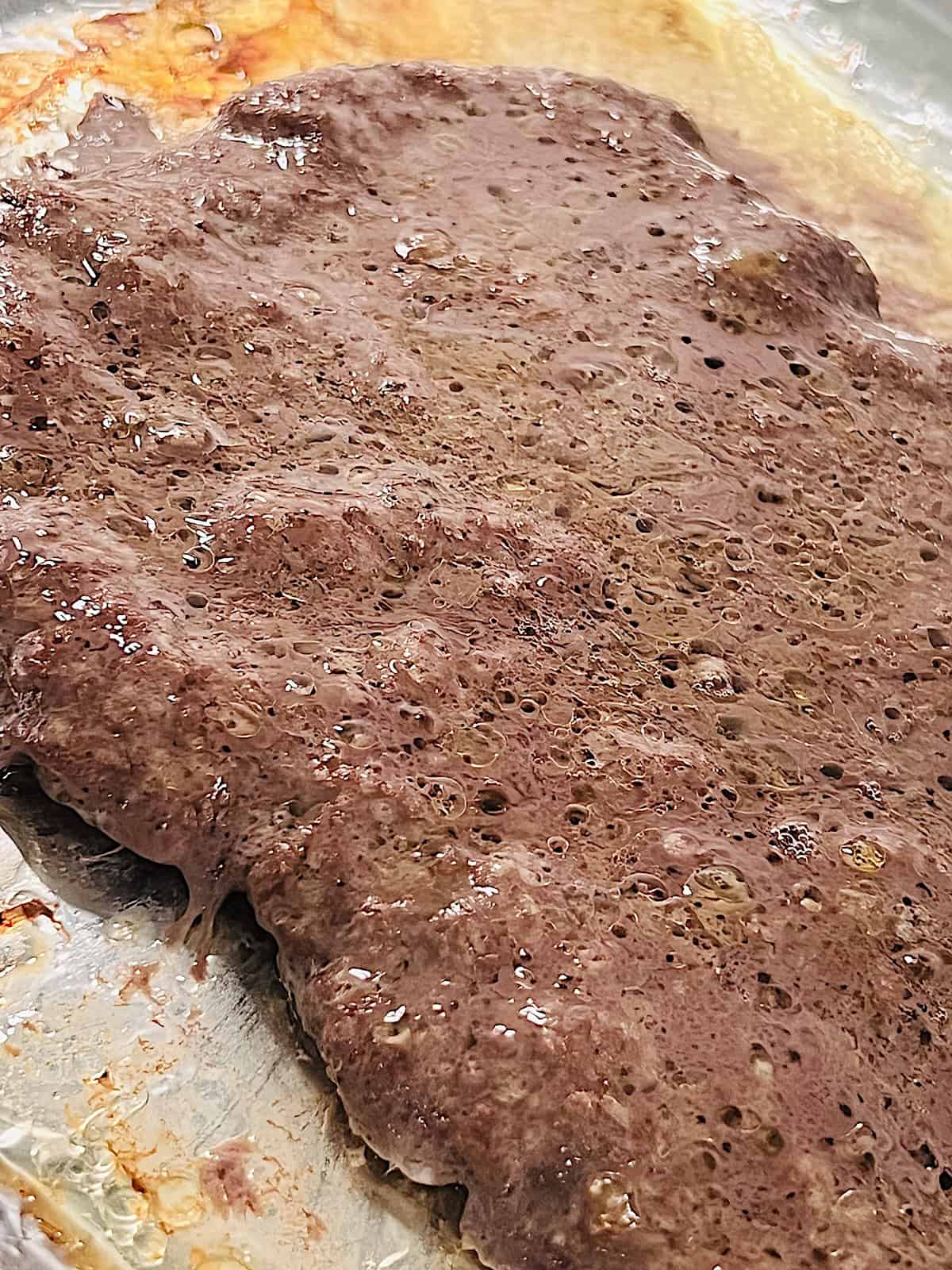 Cooked rectangle slab of seasoned ground beef on baking sheet.