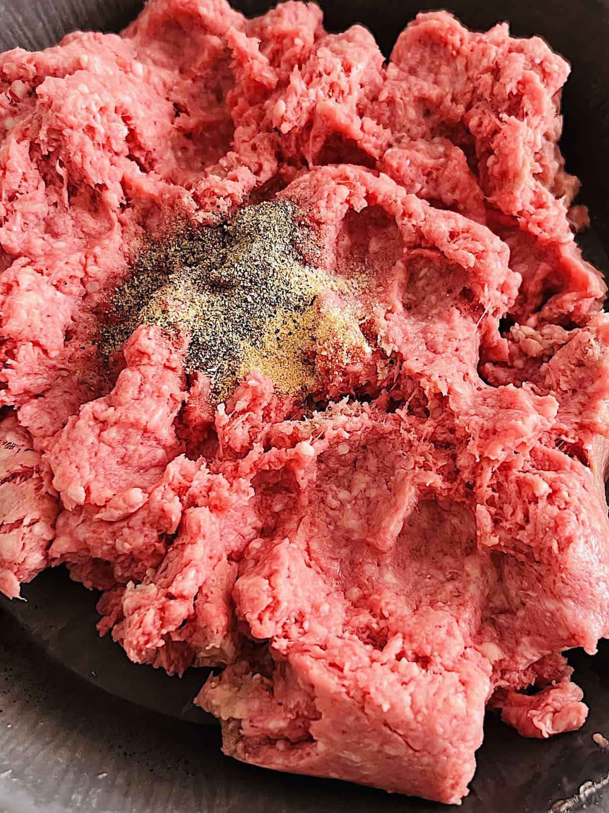 Ground beef in a bowl with seasonings.