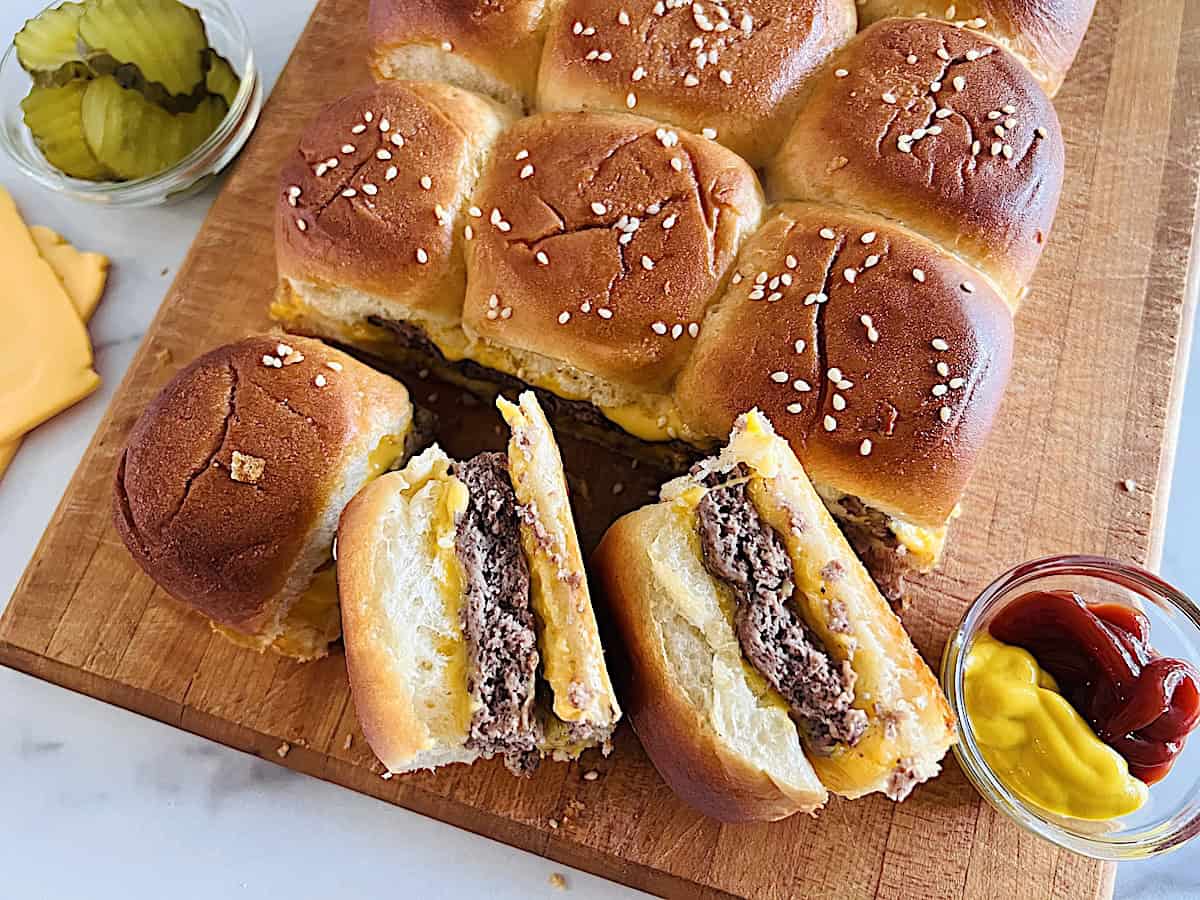 Baked Cheeseburger Sliders on Hawaiian Rolls with American cheese on a board ready to eat.