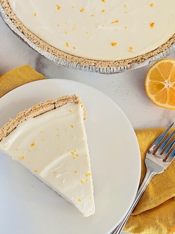 No-Bake Lemon Cheesecake Pie slice and plated next to the full creamy pie in graham cracker crust.