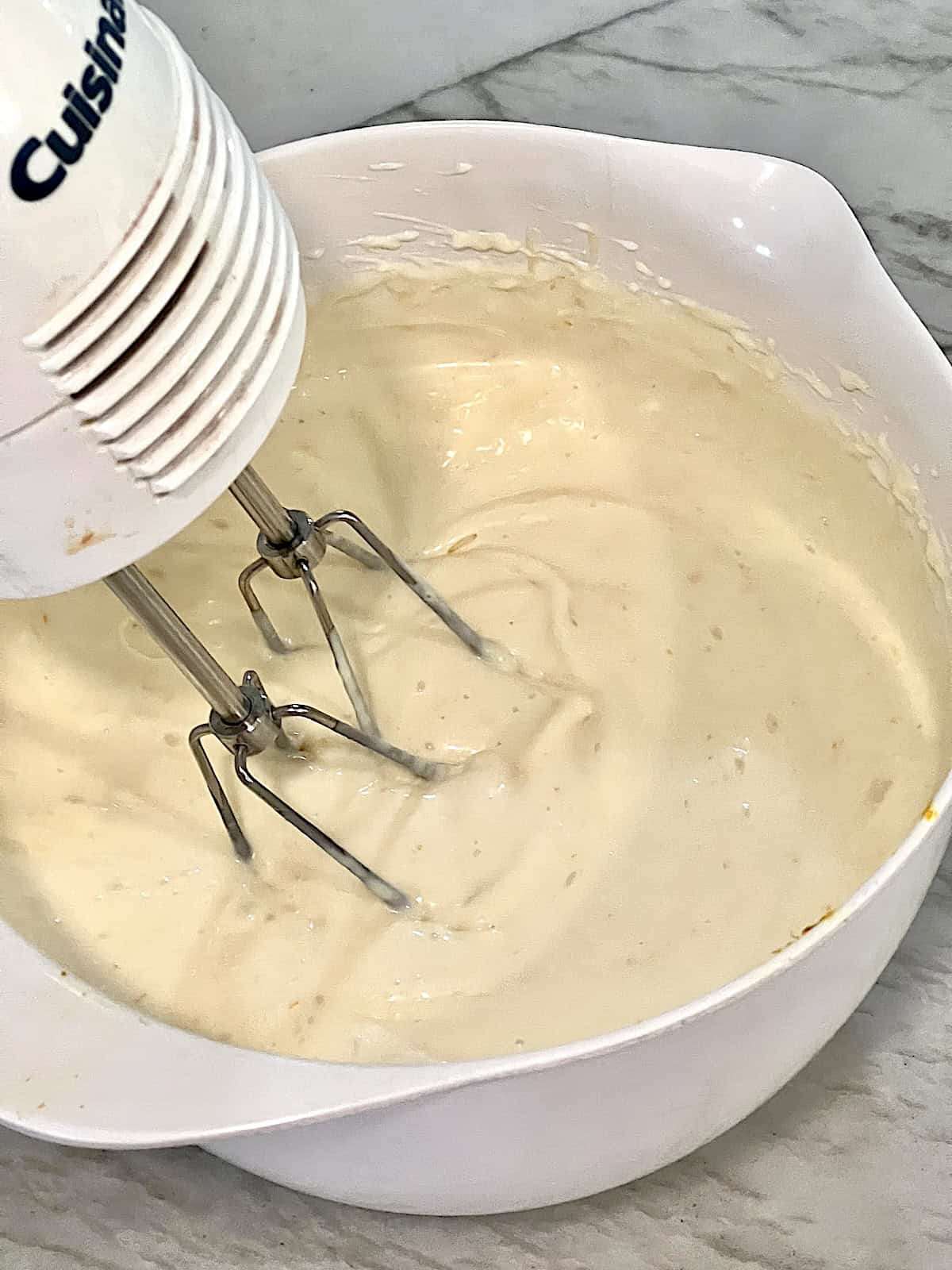 Hand mixer combining bowl of lemon juice zest cream cheese and sweetened condensed milk.