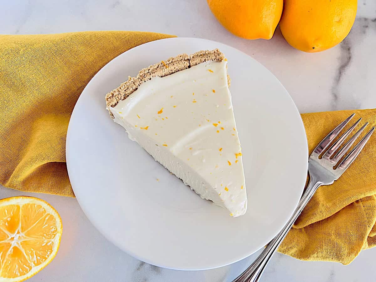 No-Bake Lemon Cheesecake Pie slice with creamy filling in in a graham cracker crust topped with zest.