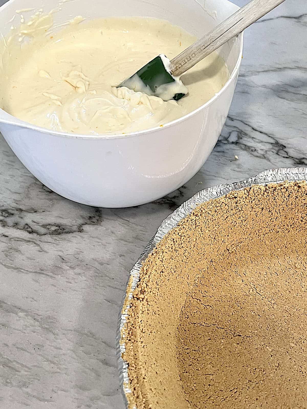 No-Bake Lemon Cheesecake Pie Lemon cream cheese condensed milk filling in a bowl next to empty crust.
