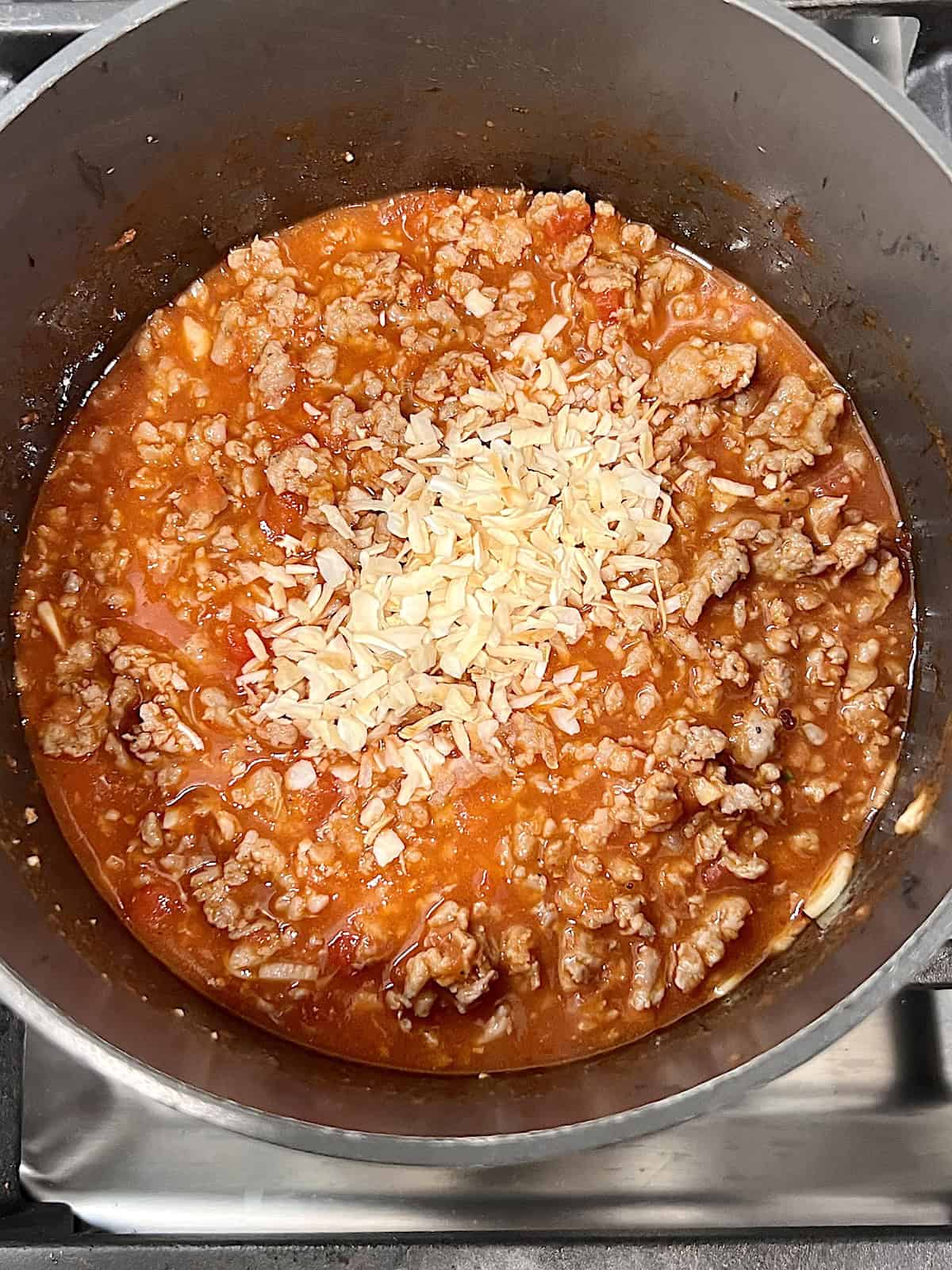 Rigatoni and Meat Sauce Adding dry onion to pot of meat sauce.