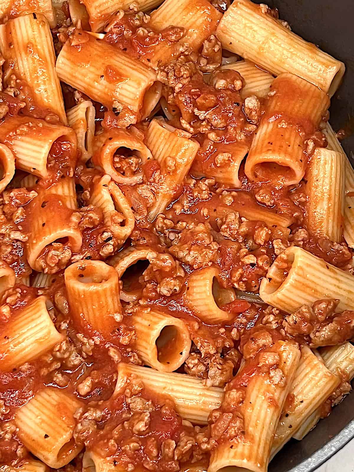 Closeup of tomato garlic ground meat sauce tossed with cooked pasta.