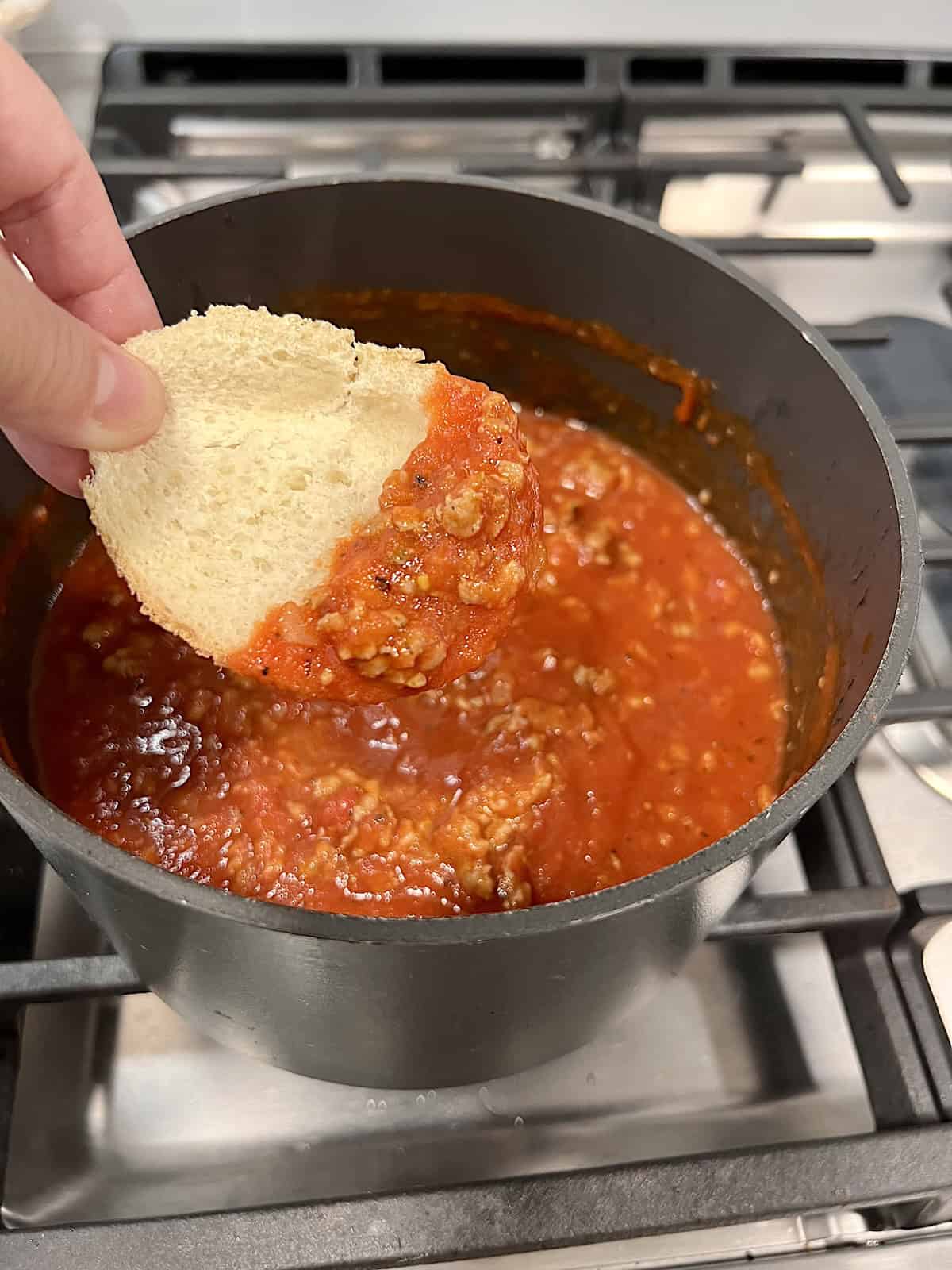 Dipping a slice of bread into the tomato sauce to taste test.