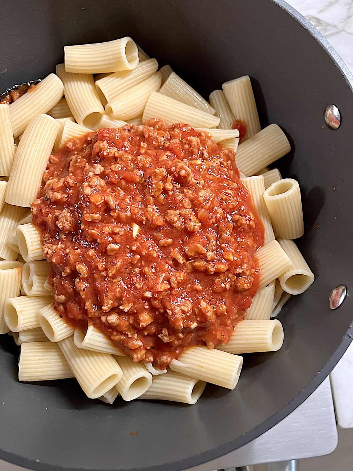 Pot with cooked pasta with pile of tomato meat sauce on top before tossingjpeg