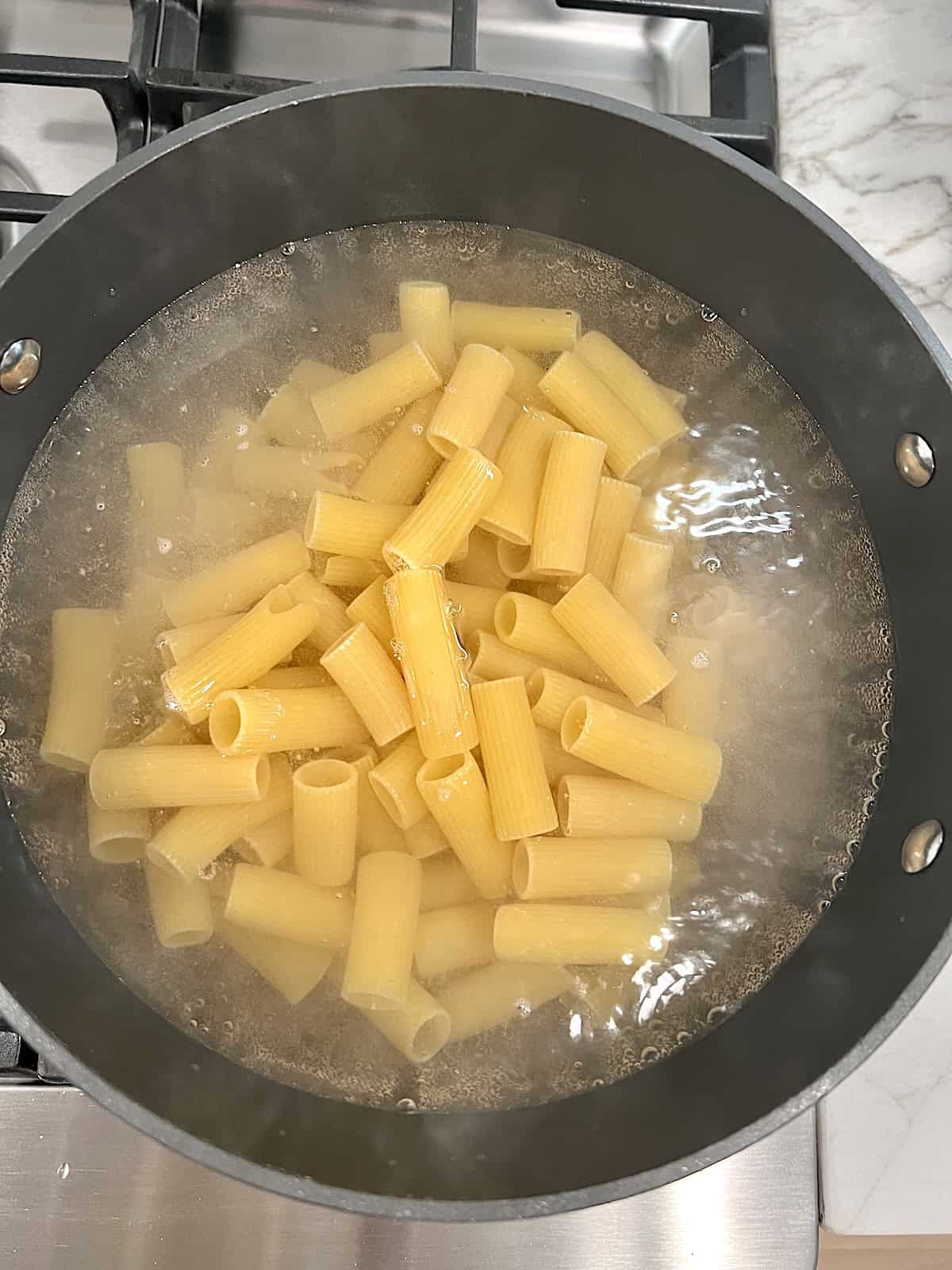 Rolling water in a pot with pasta added to cook.
