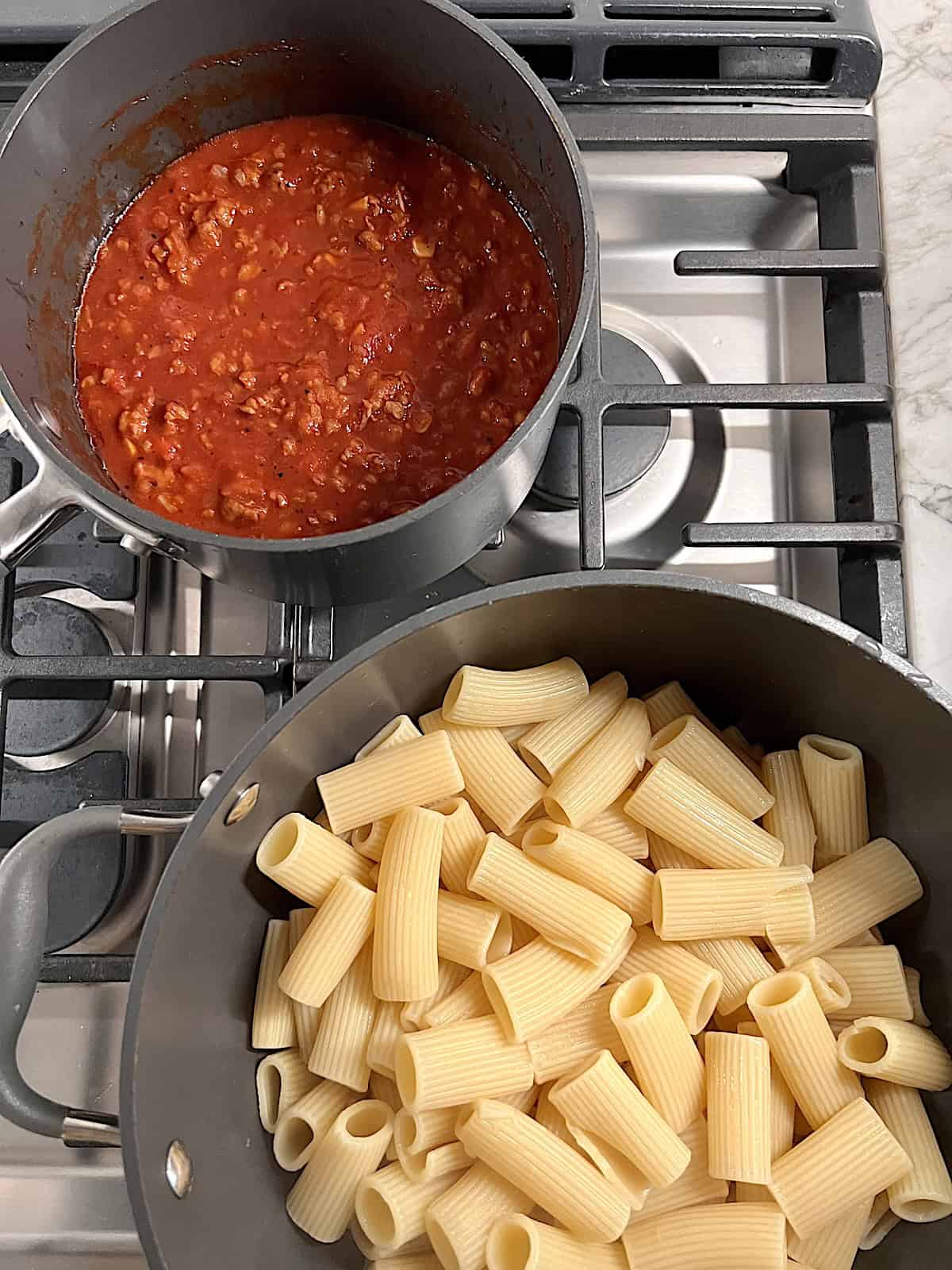 Stovetop with a pot of meat sauce and a pot of cooked pasta.