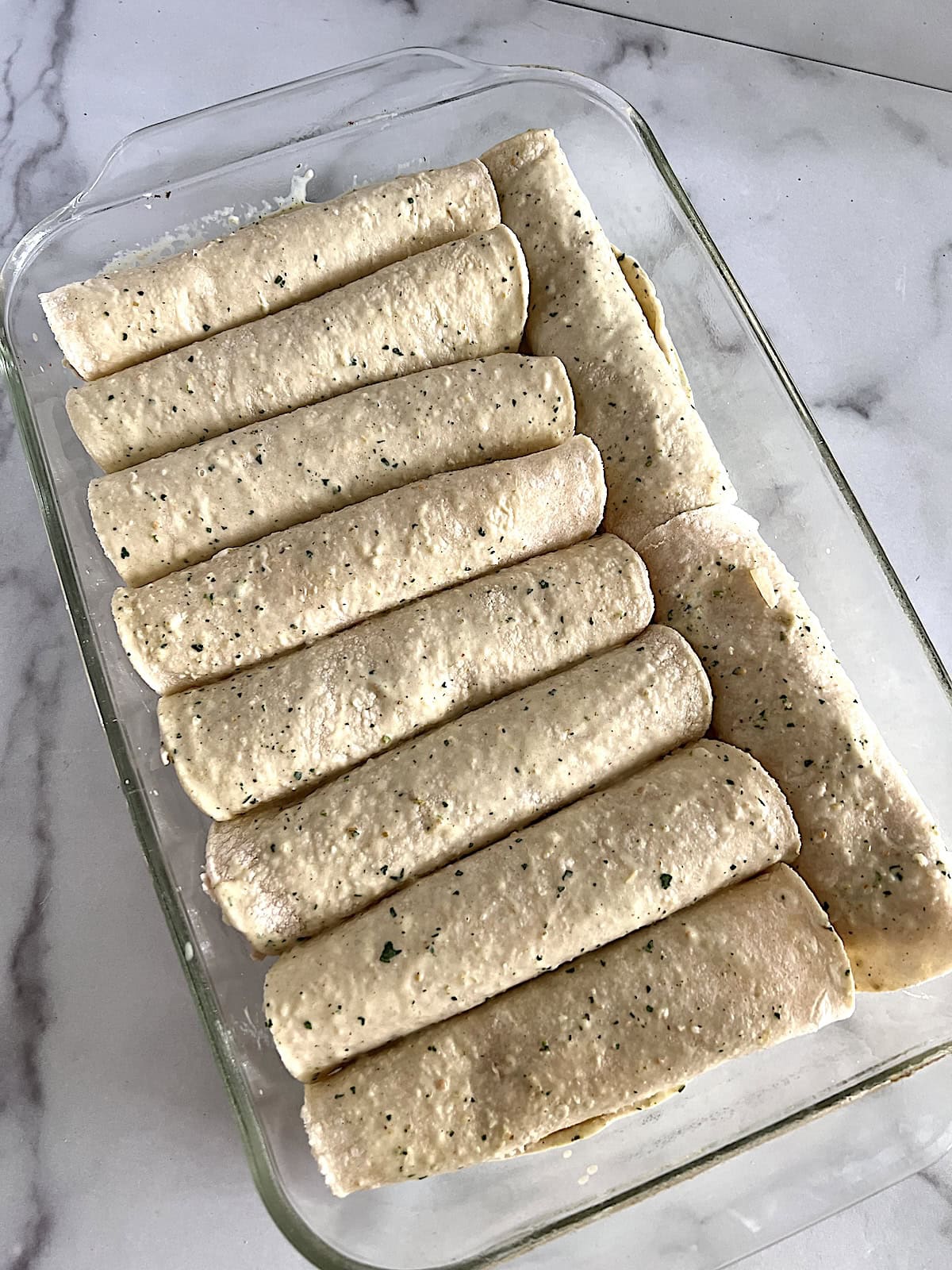 Enchiladas Suizas 10 corn tortillas filled with cheese and chicken topped in a baking dish.