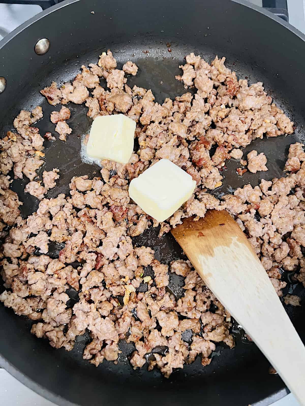 Adding butter to pan with cooked Italian sausage.