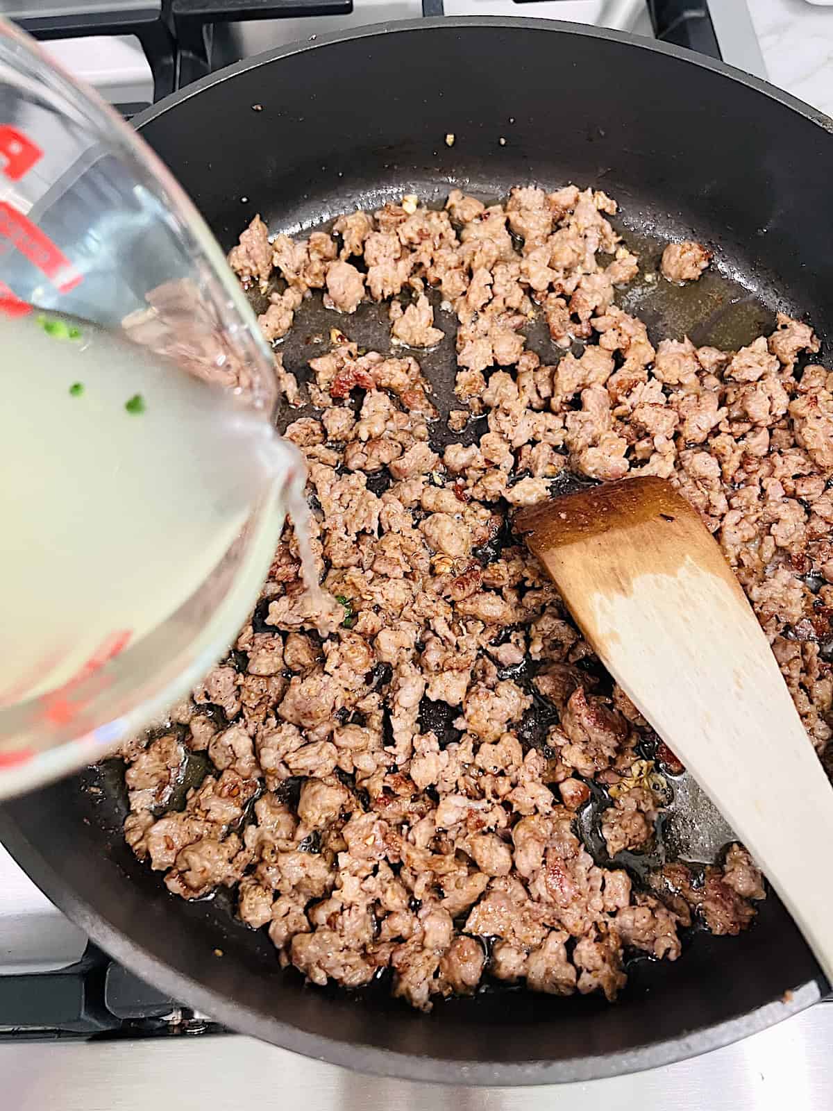 Adding pasta water to cooked sausage in pan.