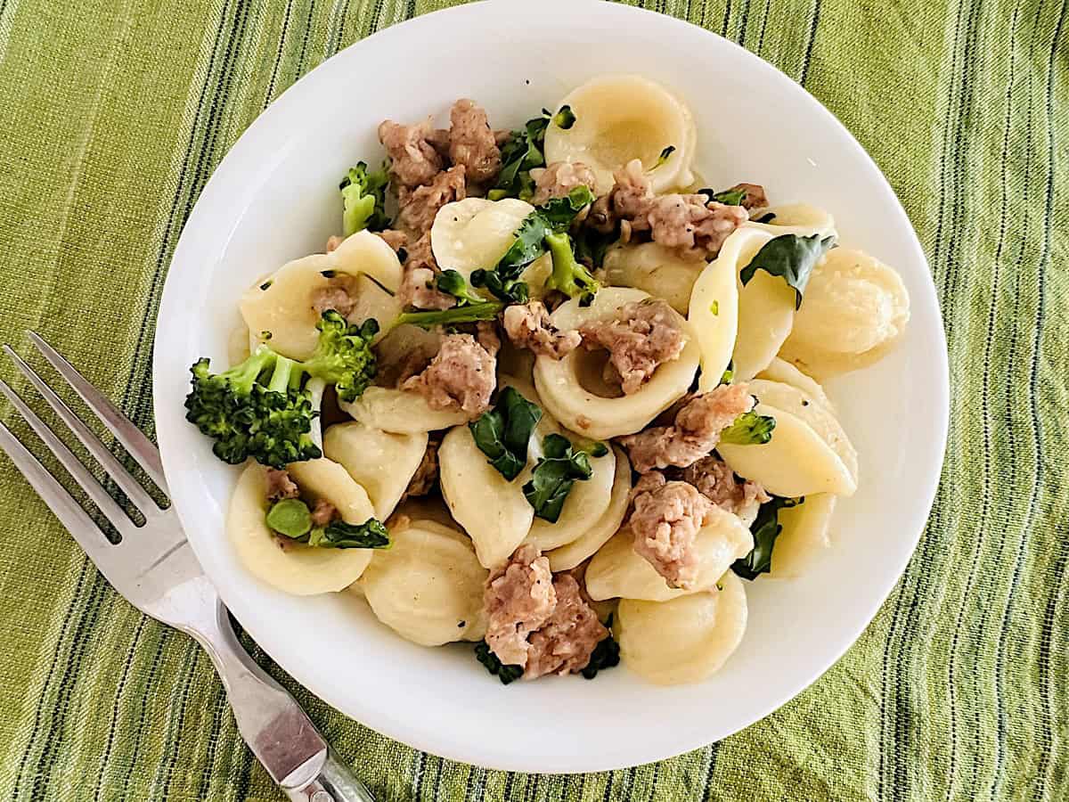 Orecchiette with Sausage and Broccoli Rabe pasta meal with crumbled sausage and greens in a bowl topped with parmesan cheese.