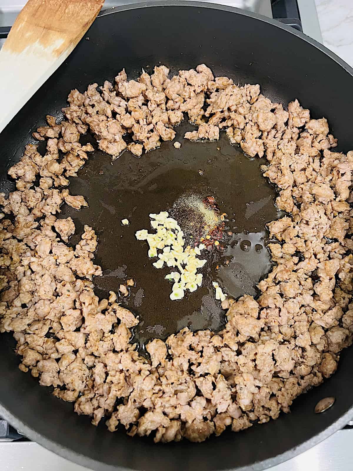 Pan with cooked sausage to the side and garlic and spices in the middle to toast.