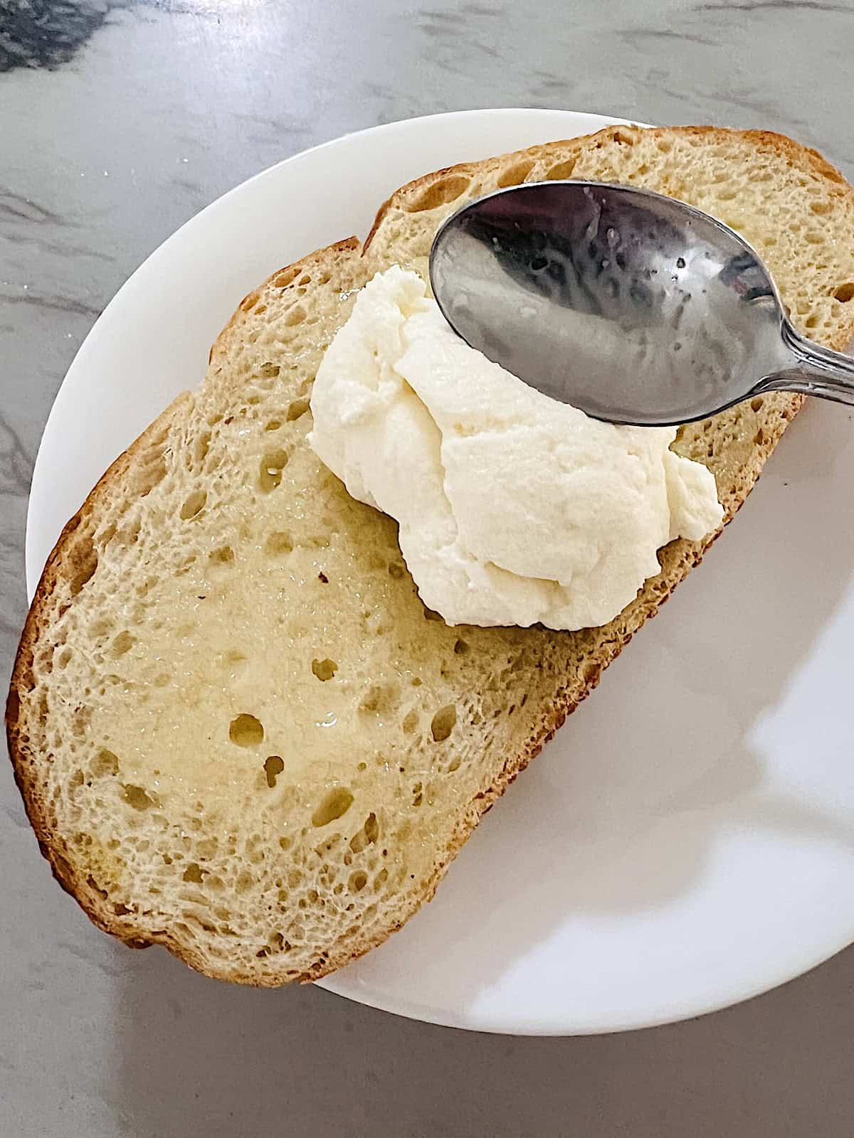 Buttered toast with spoon spreading ricotta on top.