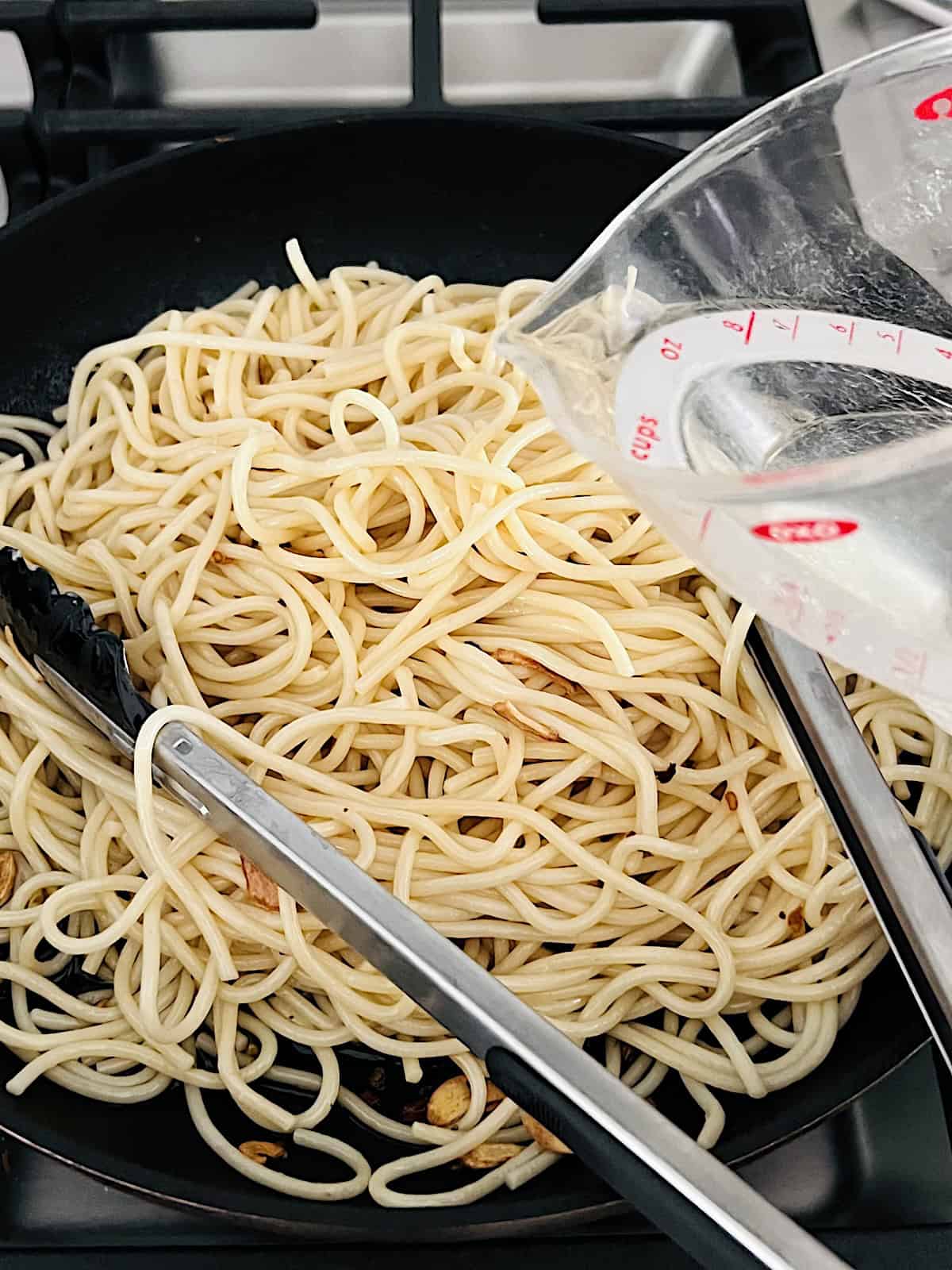 Adding cooked spaghetti and pasta water to pan with garlic olive oil and chili flakes