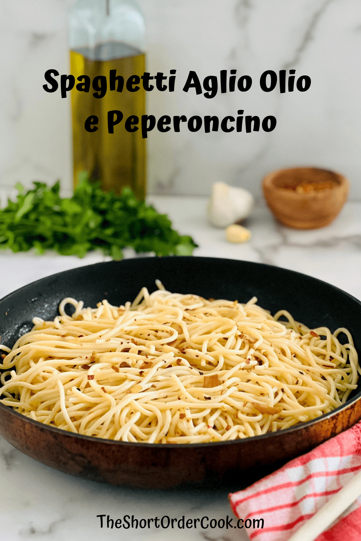 Spaghetti Aglio Olio e Peperoncino in a skillet with olive oil garlic parsley and pepper ingredients in the background.