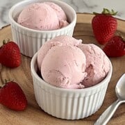 2 Bowls of Strawberry Ice Cream with spoon and fresh strawberries to the side.