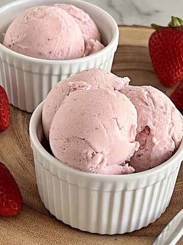 2 Bowls of Strawberry Ice Cream with spoon and fresh strawberries to the side.