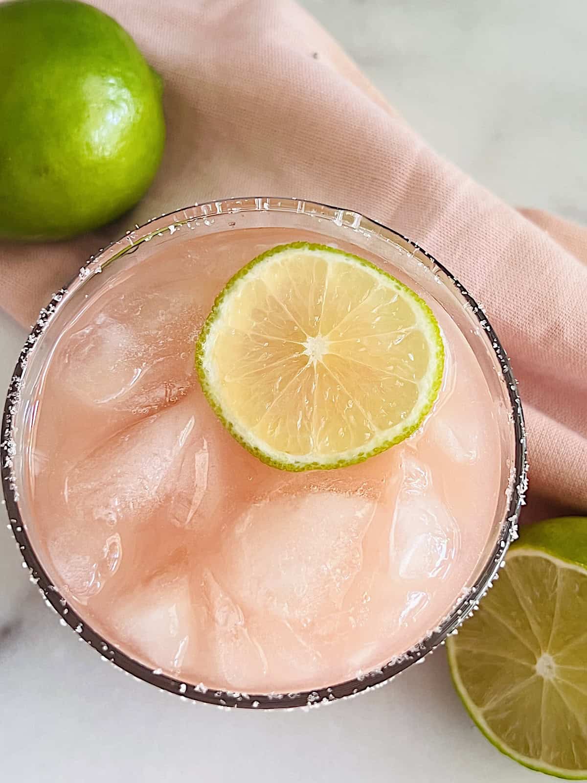 Guava Margarita Overhead of glass of pink margarita on the rocks garnished with lime slice.