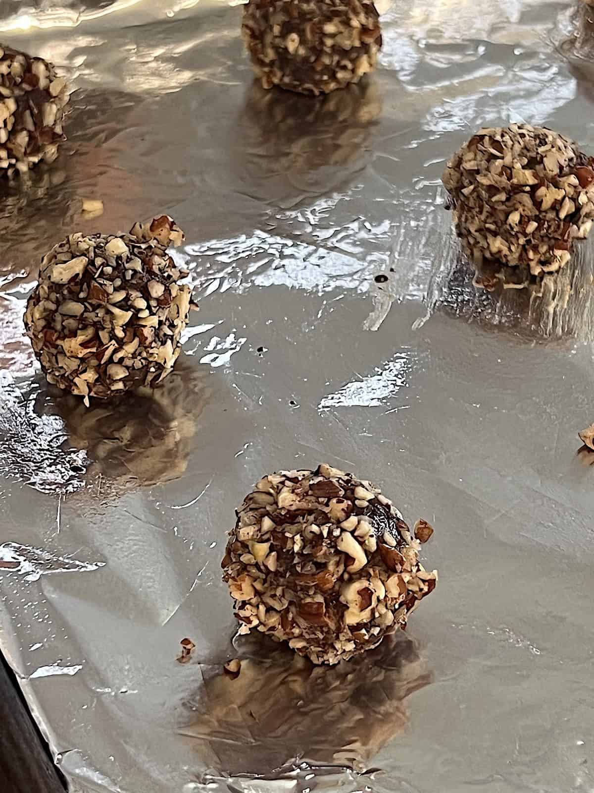 Turtle Thumbprint Cookies Balls of cookie dough rolled in pecans on baking sheet.