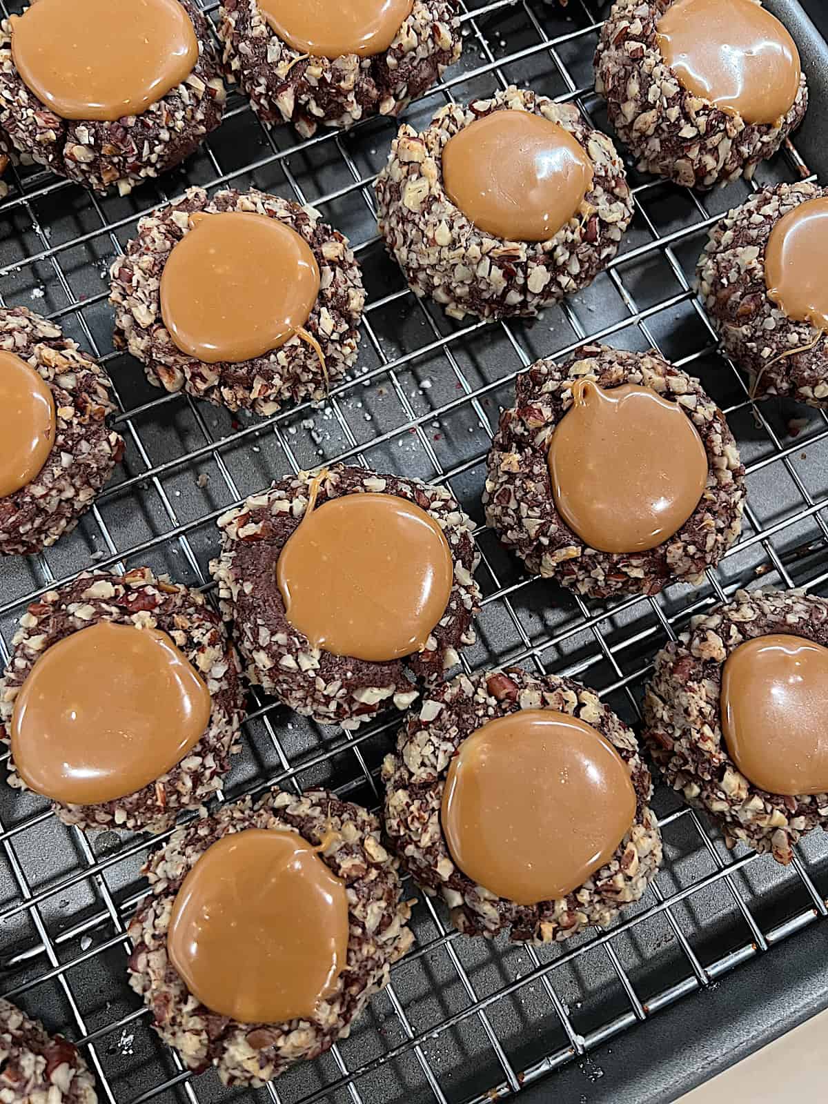 Turtle Thumbprint Cookies Fresh baked and filled with caramel resting on a rack.