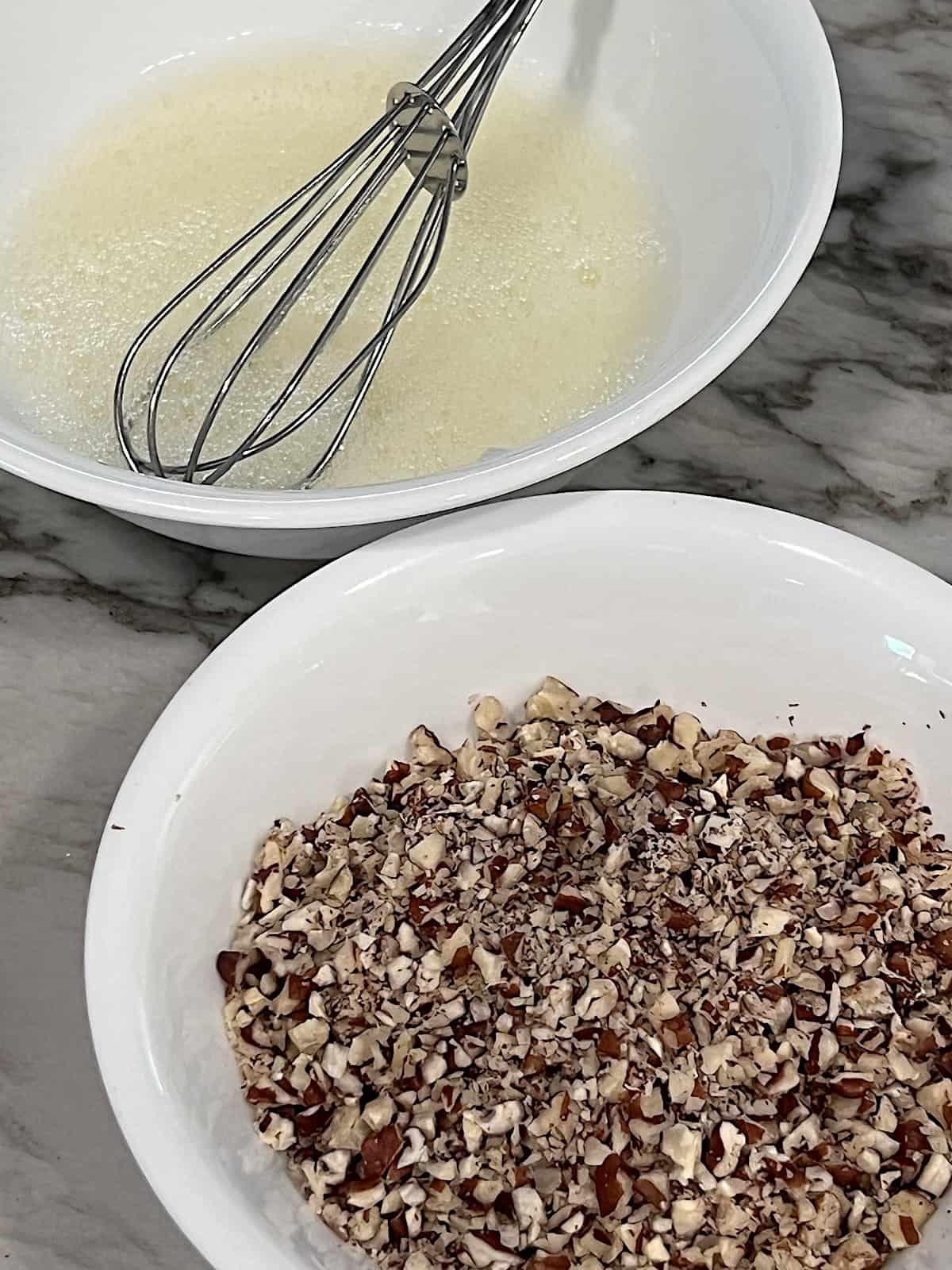 Frothy egg whites and chopped pecans in seperate bowls