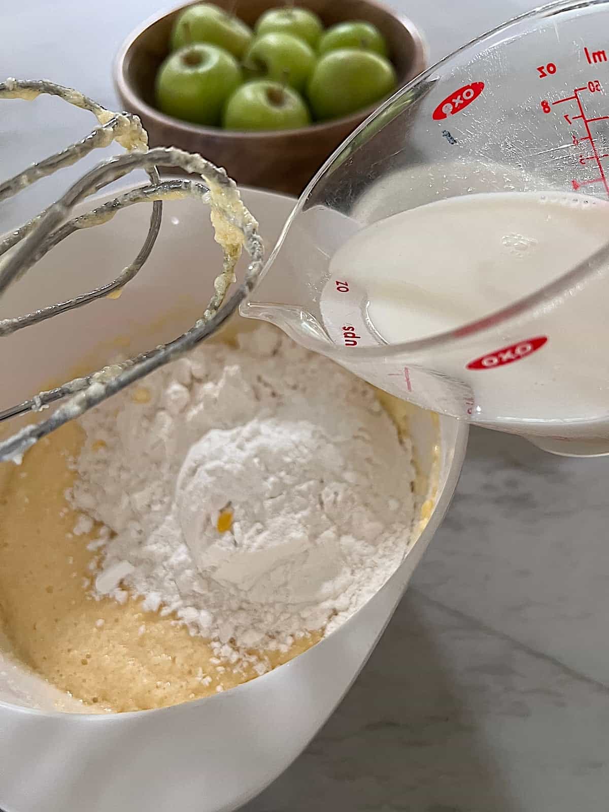 Apple Fritter Bread with Maple Glaze Adding milk to batter with flour and wet ingredients in a bowl.