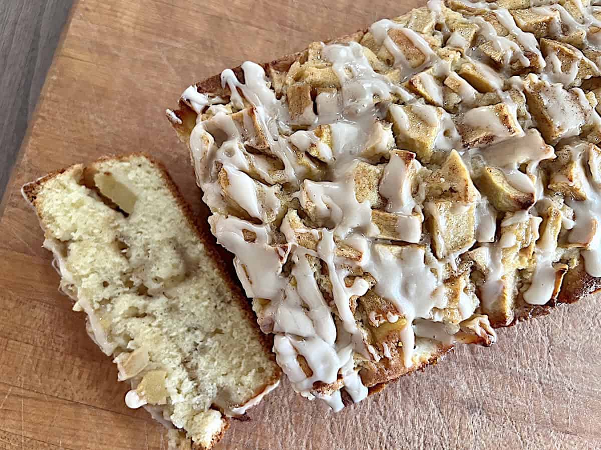 Homemade Apple Fritter Bread with Maple Glaze recipe baked in a loaf pan with diced apples & sweet drizzle on top.