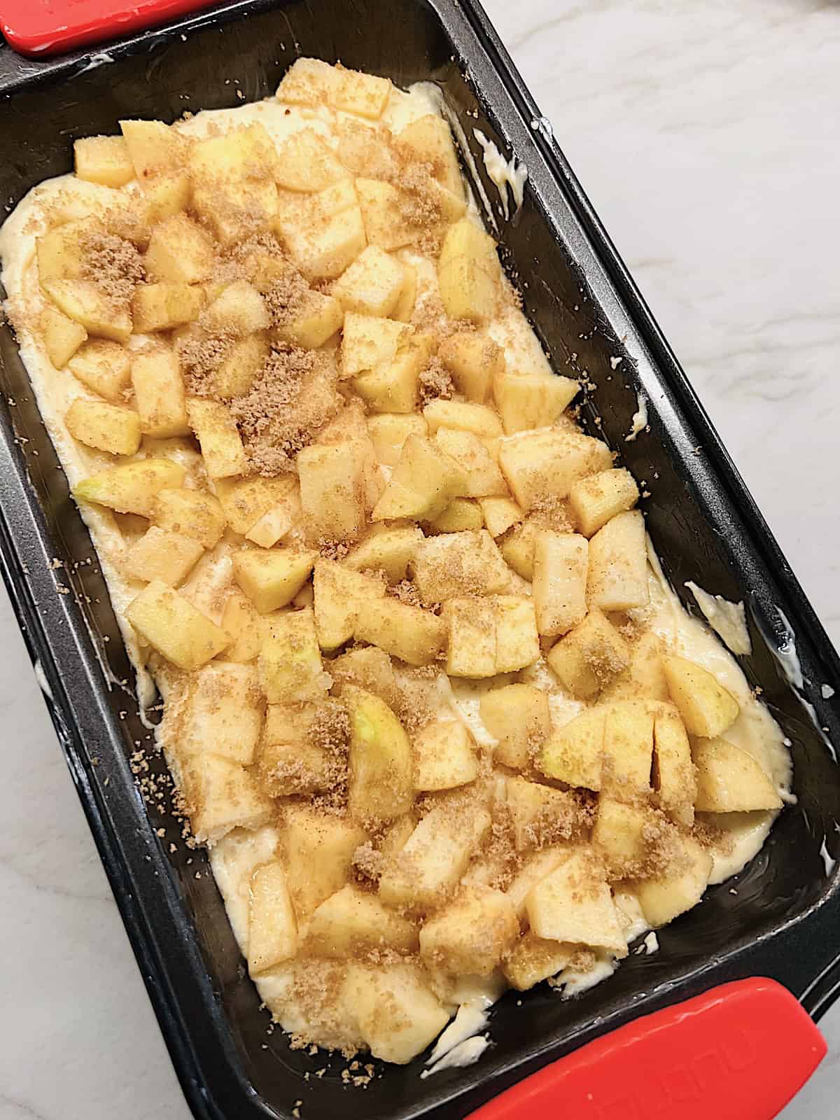 Loaf pan layered with cake batter diced apples and cinnamon sugar before baking.