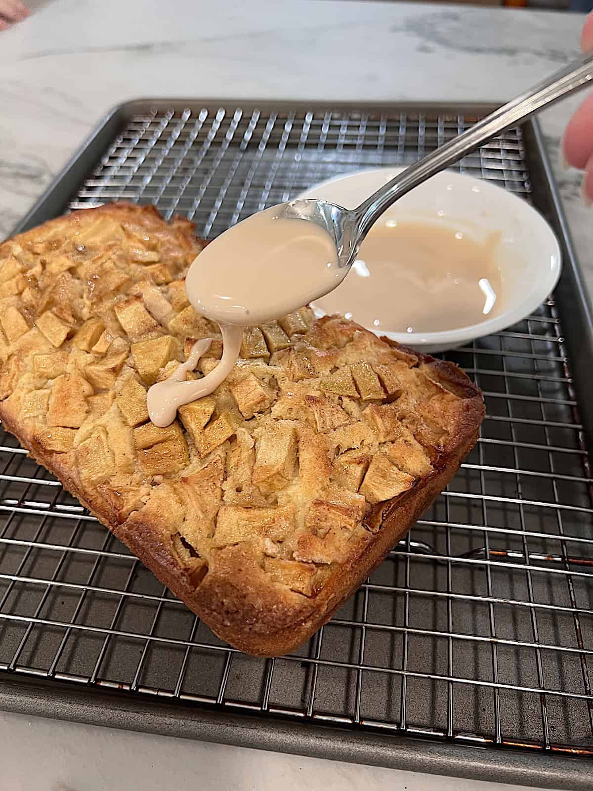 Apple Fritter Bread with Maple Glaze drizzling maple glaze on top of apple loaf cake.