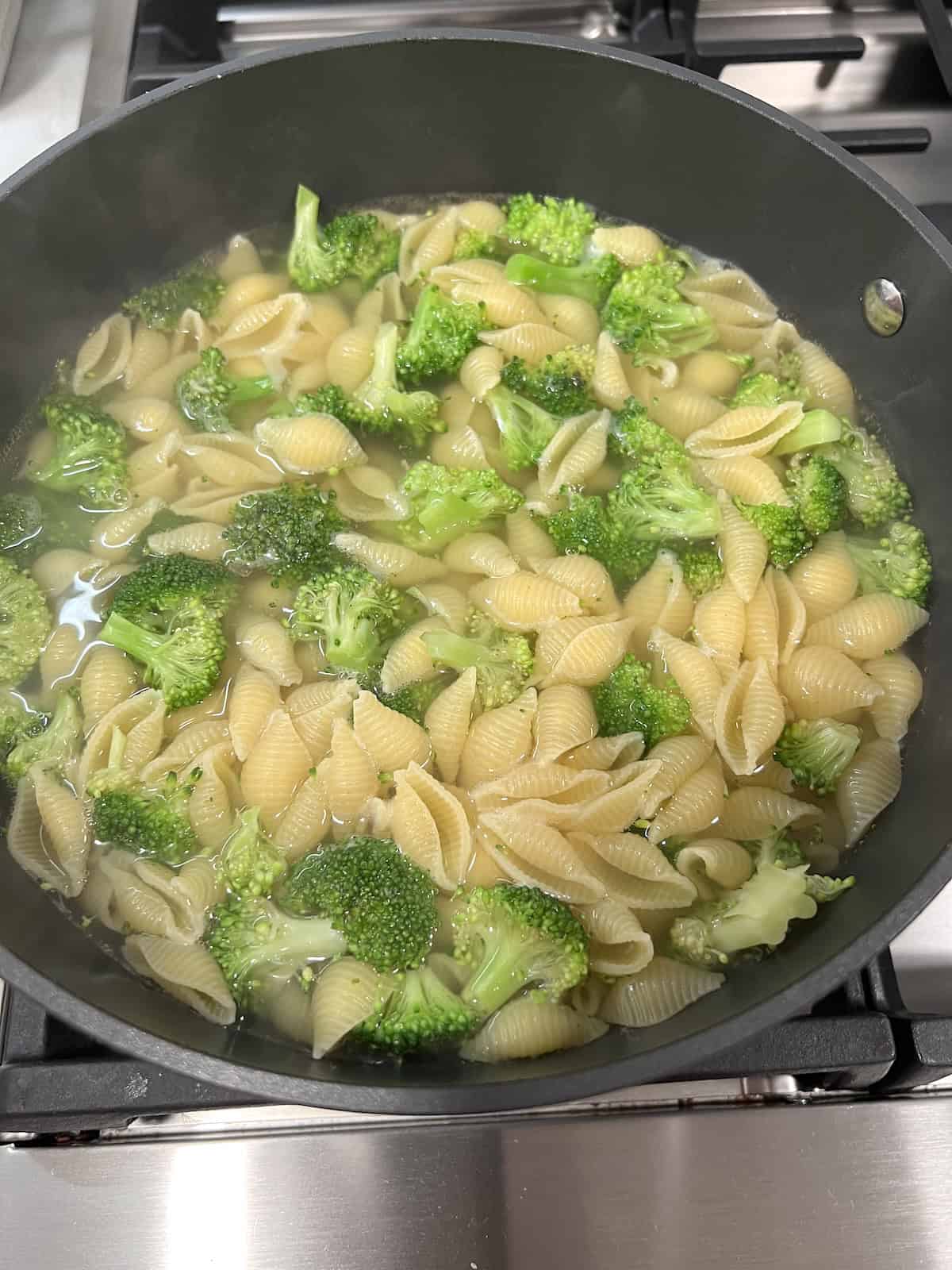 Cooking small pasta shells and broccoli florets in water in a pot.