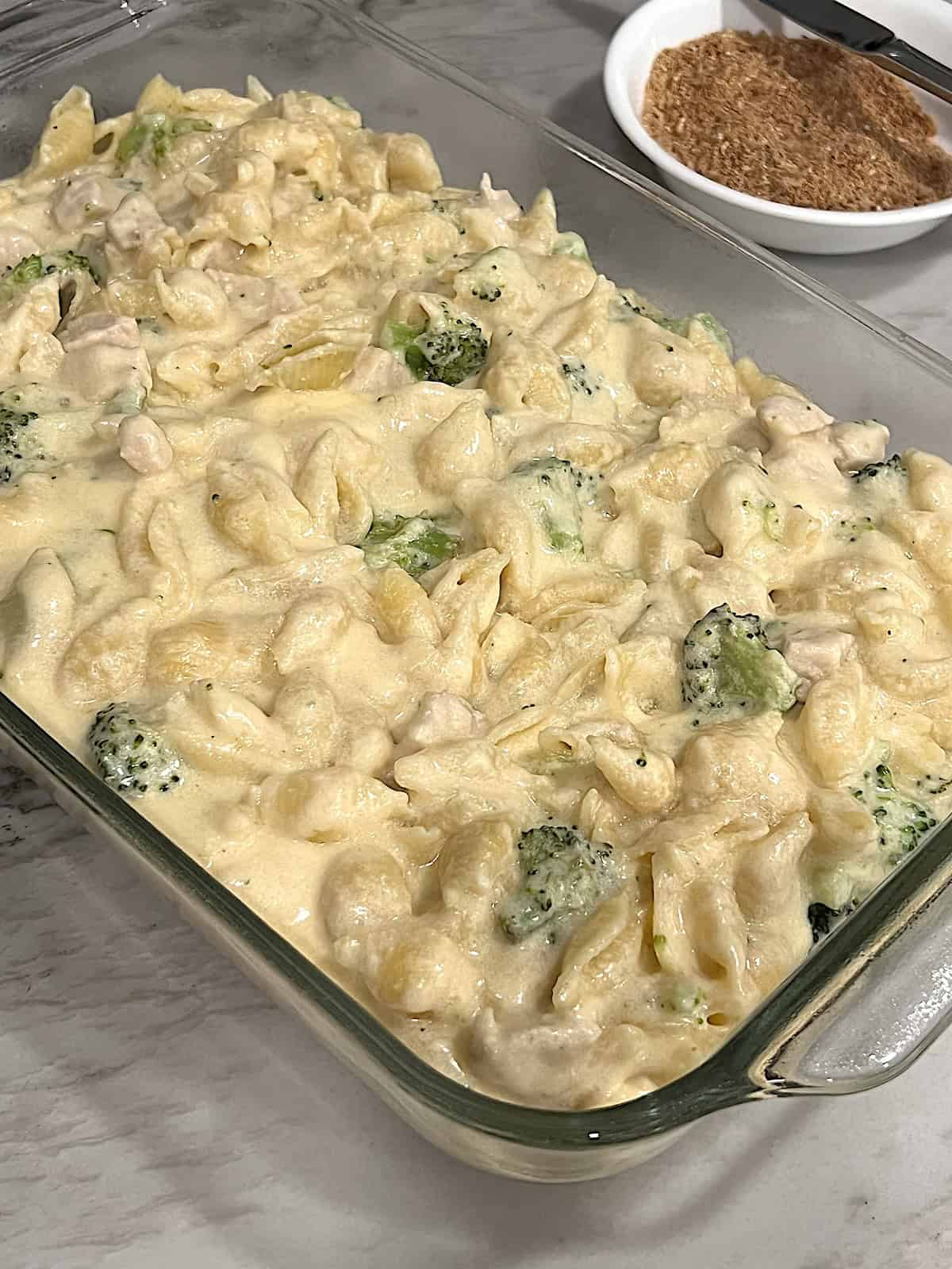 Chicken Broccoli Mac & Cheese In casserole dish with toasted breadcrumbs to the side in a bowl.